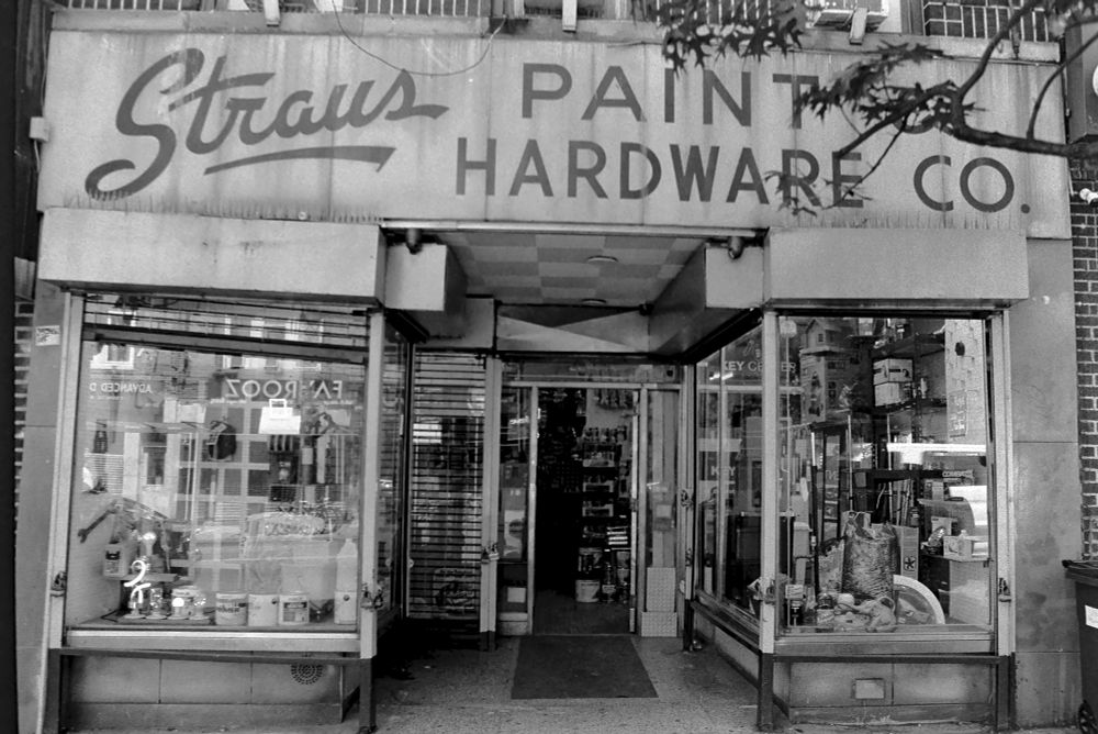 The front of an old timey hardware store called straus paint and hardware co
Glass windows show of displays of hardware