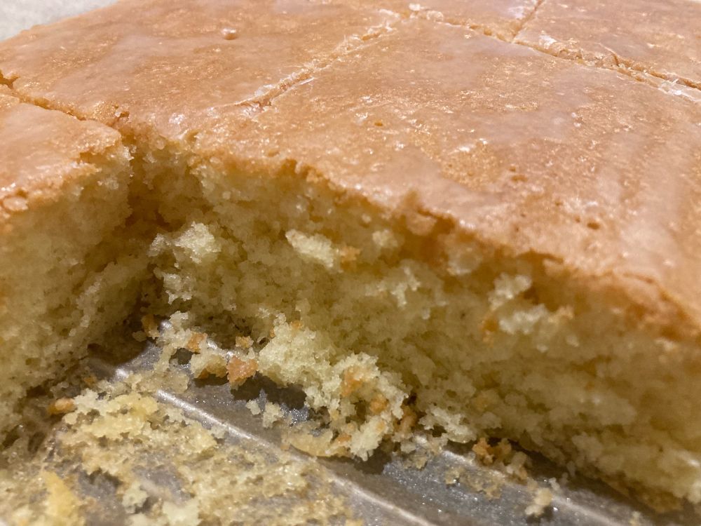 Nahaufnahme von einem Zitronenkuchen mit Puderzuckerglasur. Er ist schon angeschnitten.