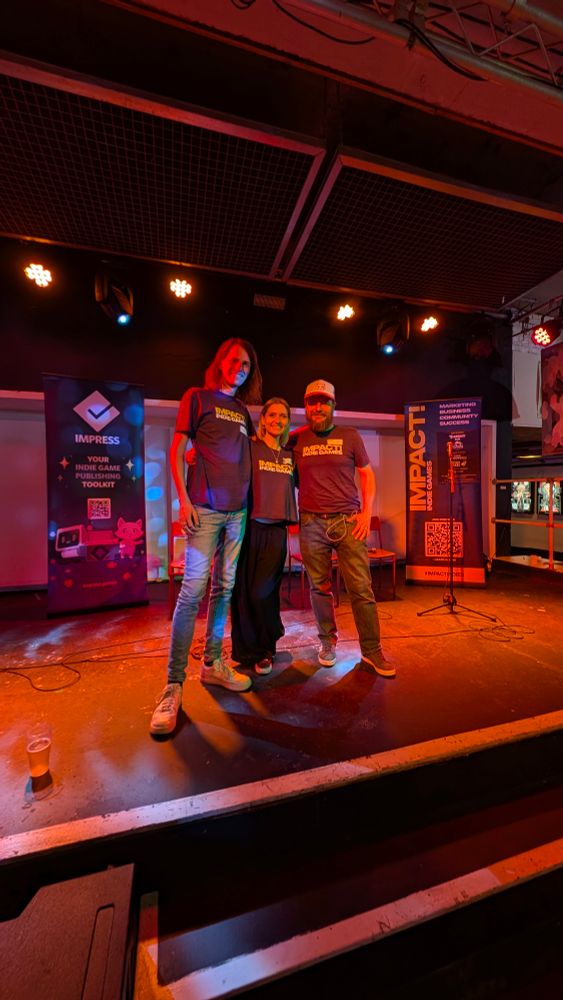 3 people on a stage. They are standing shoulder to shoulder with each other facing the camera, smiling 