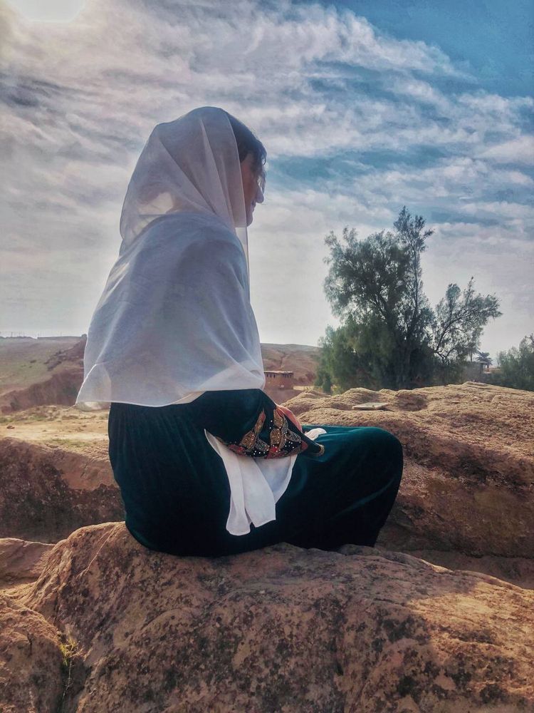 Teenage girl in traditional Kurdish dress sitting on rocks