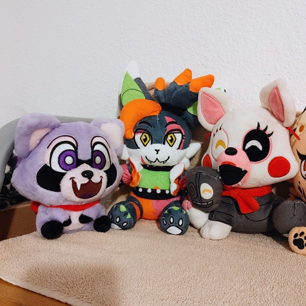 Photo of three plushies, Rambley the Raccoon, Glamrock Dusky, and Mangle FNaF sitting on a shelf. 