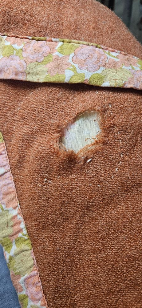 Orange-copper wool blanket with a pink and green floral cotton binding with a small hole shown.