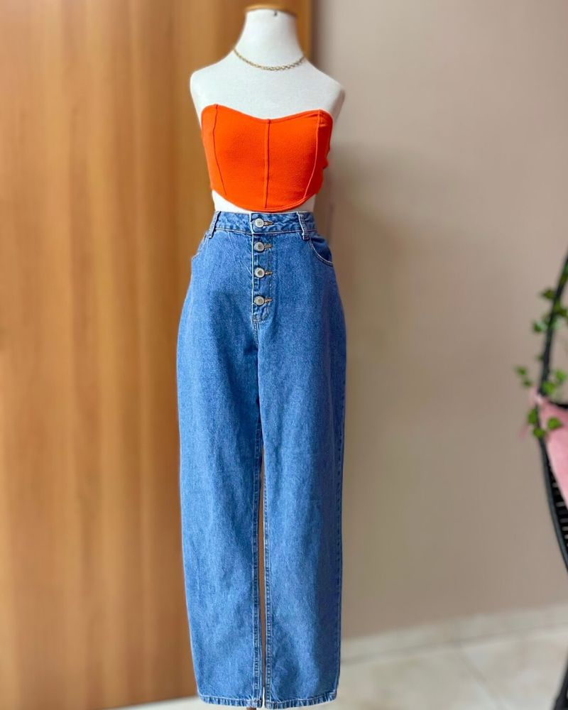 Foto de um anúncio de uma 
Calça jeans cintura alta azul claro e uma 
Cropped laranja de elastano 
Visão lateral esquerda das peças com foco aberto para ver toda a calça.
