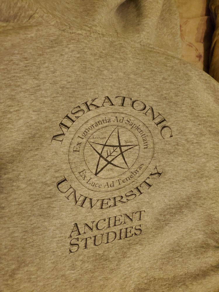 A grey hoodie with the Miskatonic University Ancient Studies logo on the back
