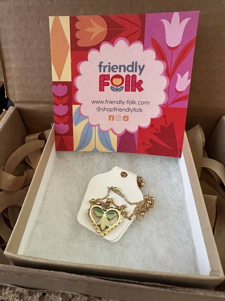Cute heart necklace with a flower design in a box with the colorful Friendly Folks logo.