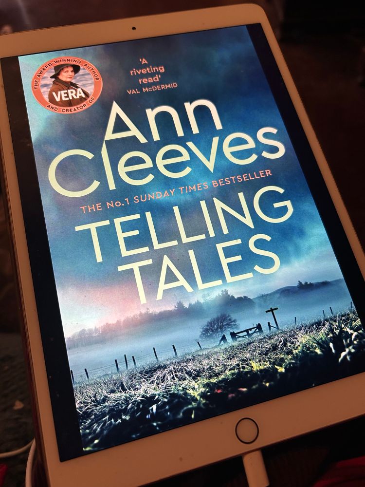 iPad with an e-book

Ann Cleeves
TELLING TALES

Most of the cover is moody dark sky. At the bottom of the image a flattish landscape is divided by a broken down wire fence with a gate just off-centre. 