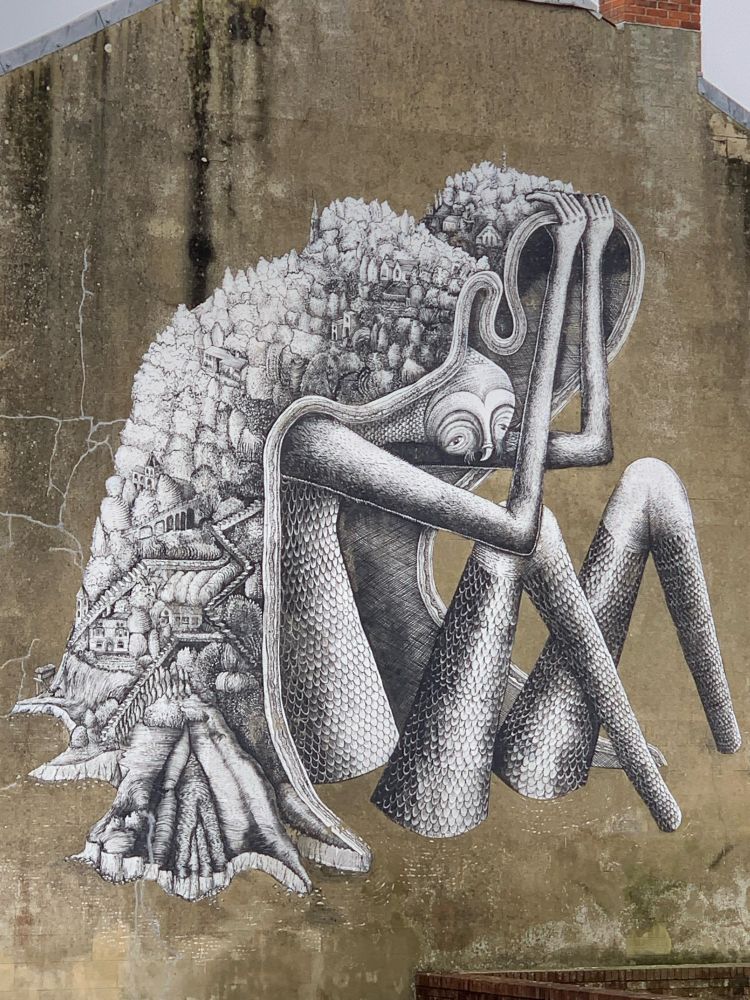 Street art of a fish woman whose hair depicts the rise of a hill from cliffs to top.