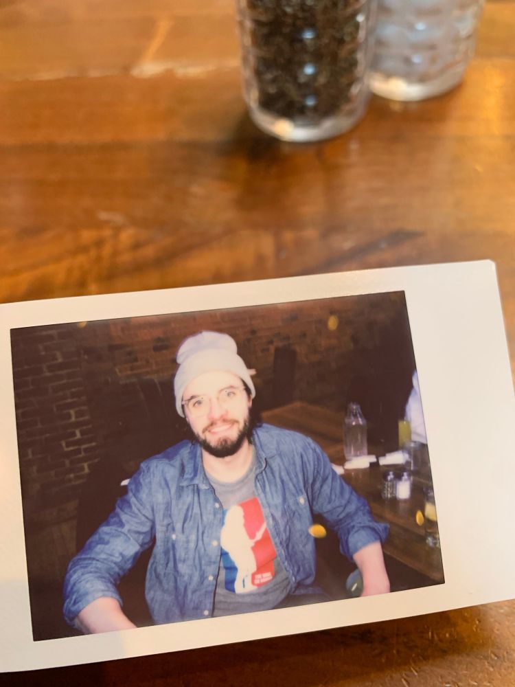 Photo of me sitting in a bar wearing a winter hat and glasses, a The War on Drugs shirt that looks like the NBA logo, and an unbuttoned button down shirt