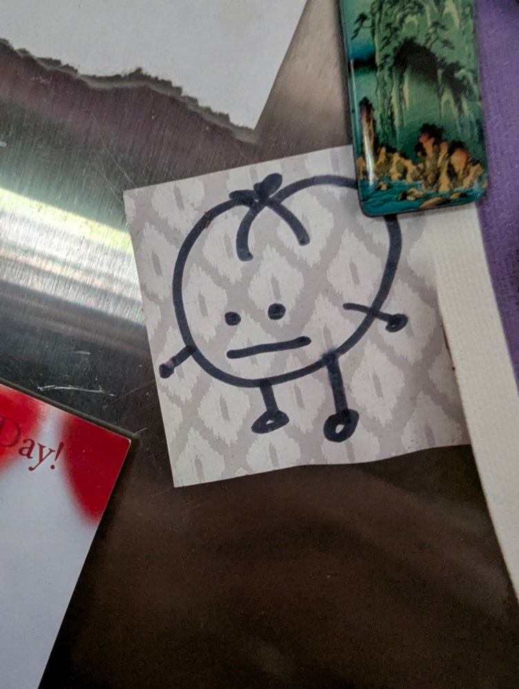 Line sketch of a 'little tomato guy' on patterned paper. Stick arms and legs but this little fucker has some rizz going on with it.  So it was hung on the fridge to see its expressionless face for entertainment 