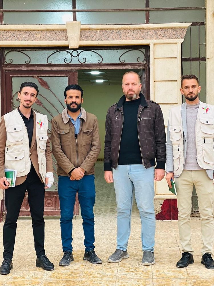 Four members of the Youth Peace Team within Ba'aj district, Iraq, stand in front of a school that they advocated to reopen. This initiative was supported by NP. 