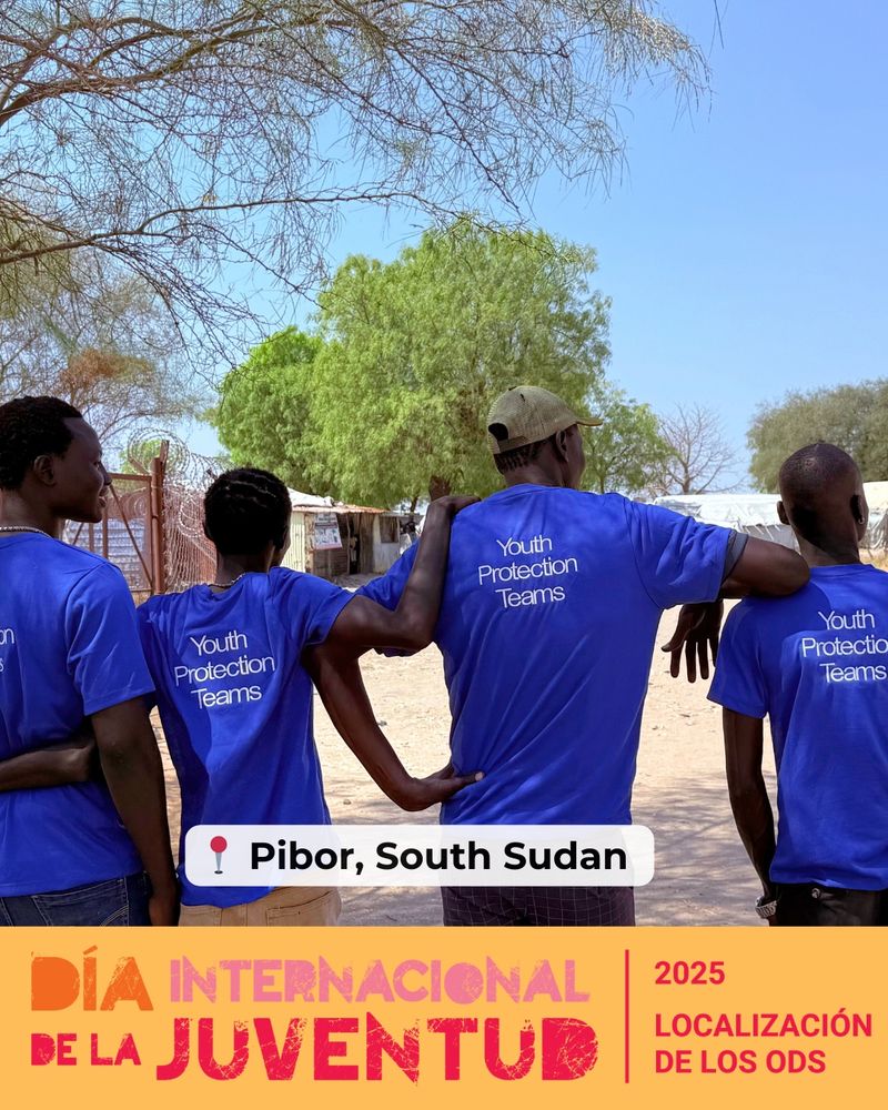 Four youth stand outdoors with their back to the camera and arms linked around each other’s shoulders. They are wearing blue t-shirts that read “Youth Protection Teams” on the back. Location tag reads “📍 Pibor, South Sudan.” Pink and orange text at the bottom says “DÍA INTERNACIONAL DE LA JUVENTUD” with “2025 Localización de los ODS” in the right corner.
