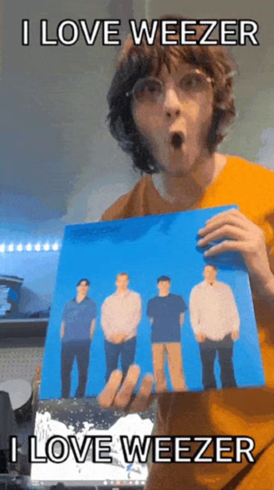 a man in an orange shirt is holding a picture of weezer in his hand