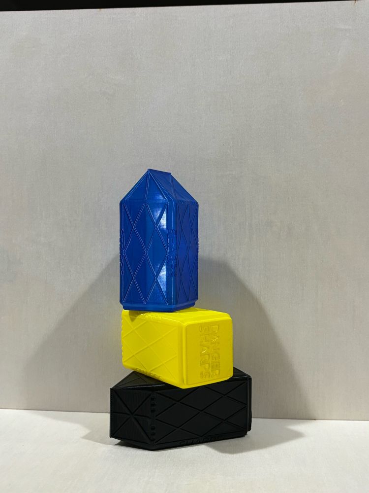 Three little boxes that look like small milk cartons. They are colored black, yellow, and blue. They are stacked on top of each other.