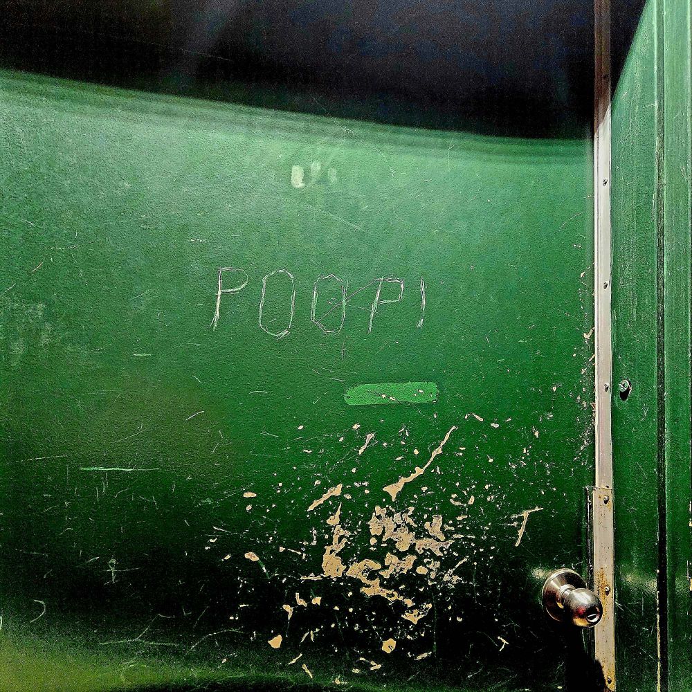 Green door with the word POOP! scratched into the paint