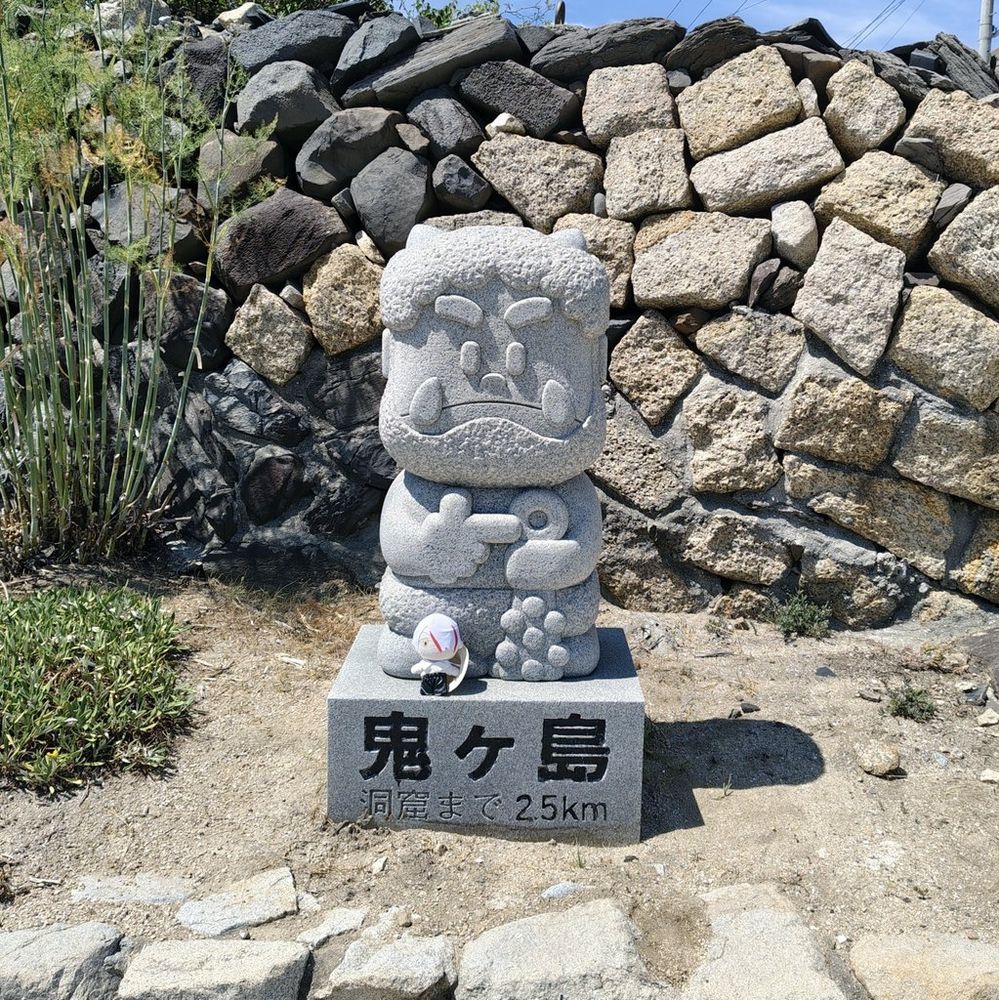 鬼ヶ島大洞窟への方向と距離を示す鬼の石像の前に、ゼロさんのぬいぐるみが置かれている。