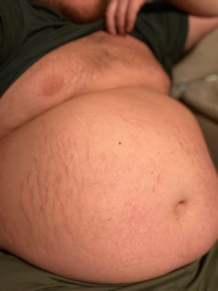 Large fat man sitting down and lifting his shirt. Exposing his large belly covered in stretch marks.