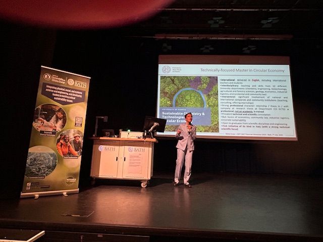 Prof Silvia Gross stands on the stage in front of a PPT for a plenary talk on inorganic chemistry and its role in addressing future global challenges in the energy transition.