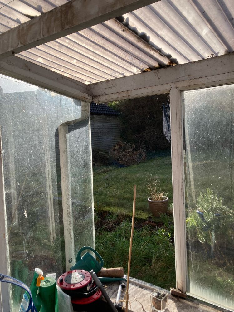 The corner of a shonkily built lean-to, missing part of a window frame and a pane of glass