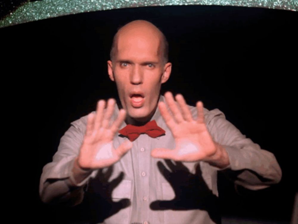 a bald man wearing a red bow tie is making a stop gesture with his hands