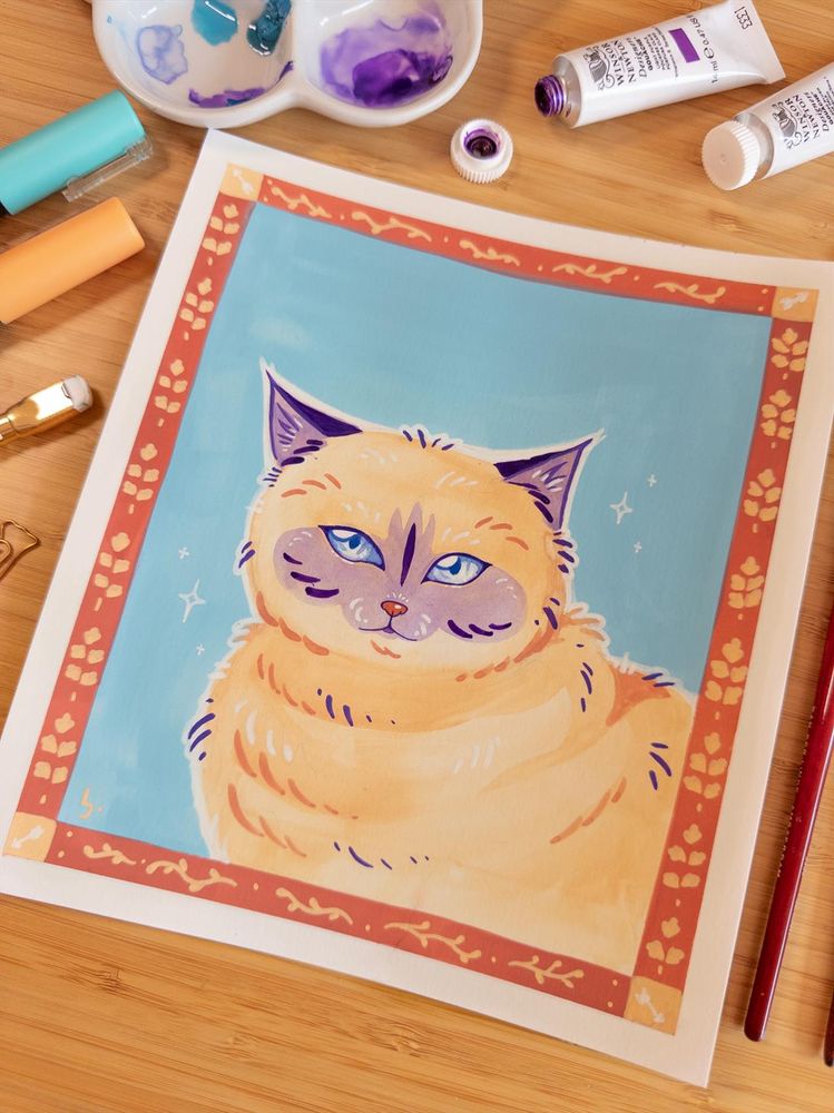 A colorful portrait of a cat made in gouache and posca markers. The cat is beige with purple shadow markings in it's snoot and on it's ears. The drawing is surrounded by traditional art supplies like markers, paint tubes and brushes.