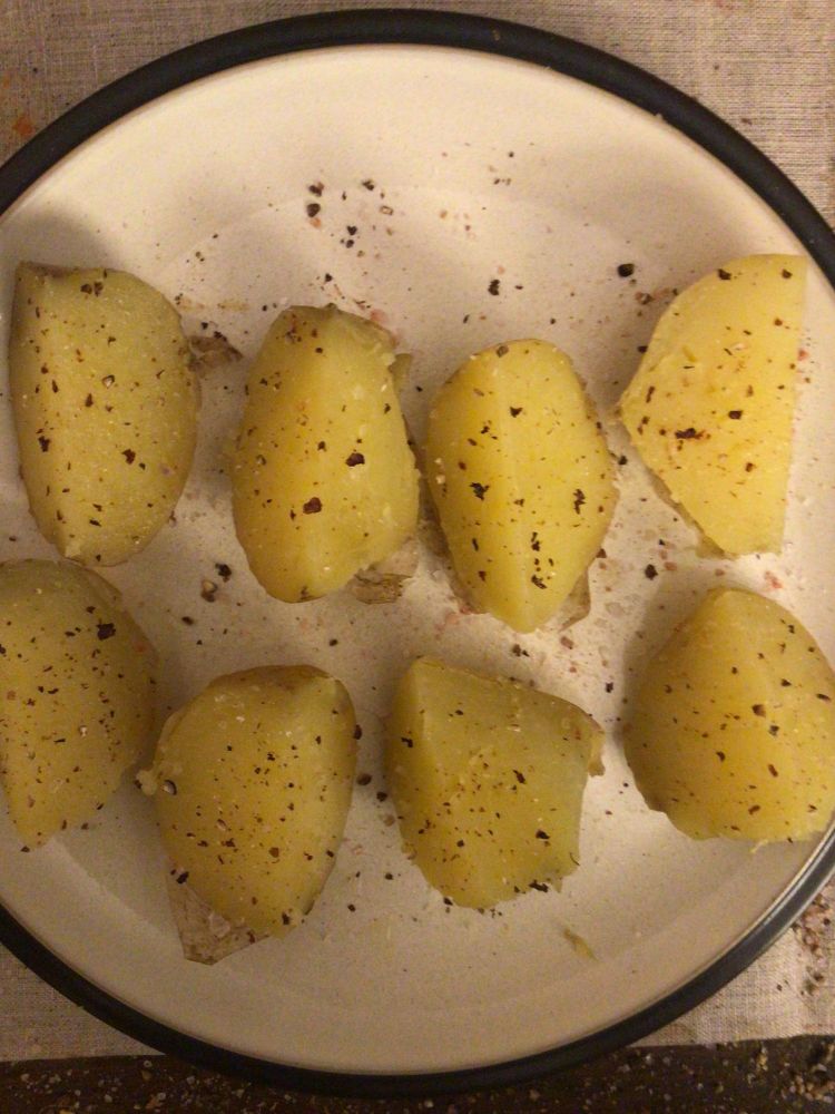 Two Yukon gold potatoes cut into quarters and seasoned with salt and pepper on a dinner plate