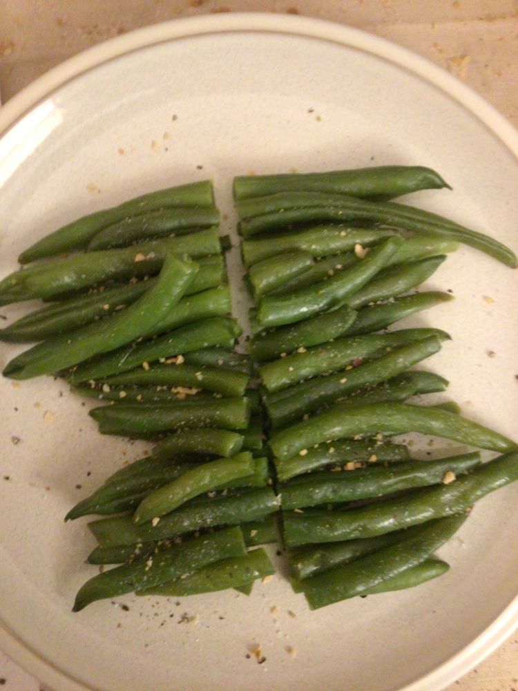 A good portion of green beans seasoned with salt, pepper and minced garlic on a beige dinner plate