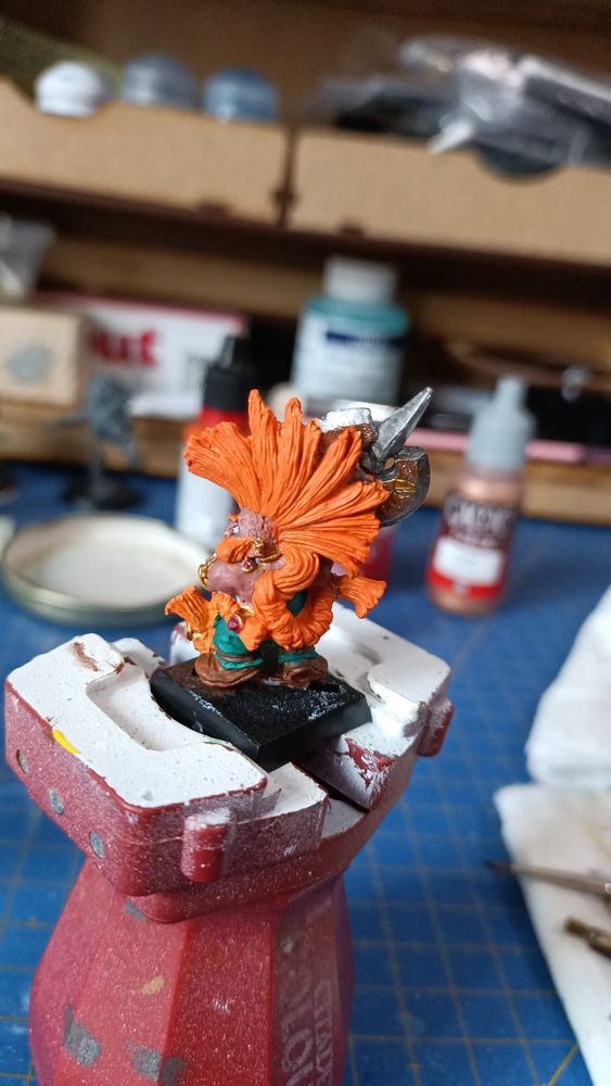 Foto de un matademonios de Warhammer Fantasy, con cresta y barbas trenzadas en naranja, múltiples adornos en oro y con un hacha de doble filo labrada con símbolos visto por detrás 