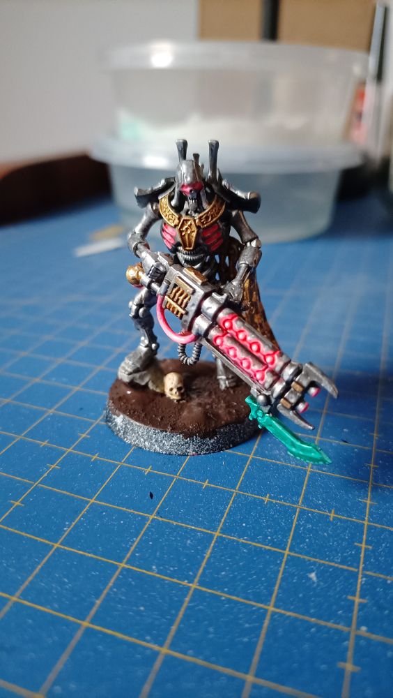 Vista del necrón de frente con el color fluo de energía del arma reducida a los surcos y aberturas, el resto en metal plateado con detalles en oro y cables fluo