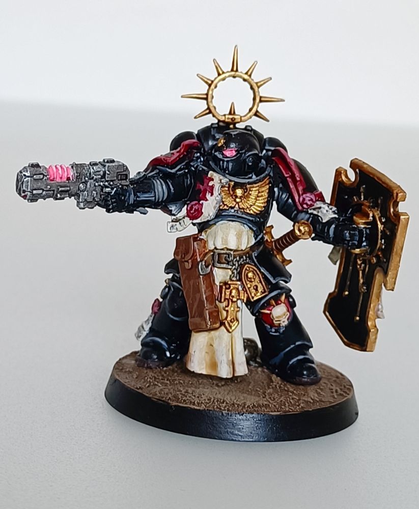 Foto de una miniatura de Warhammer 40k de un teniente primaris bladeguard armado con un bolter, escudo y espada al cinto, con armadura negro sólida perfilada en los relieves y ropajes blanco sucio, propia de los templarios negros. Vista por delante 
