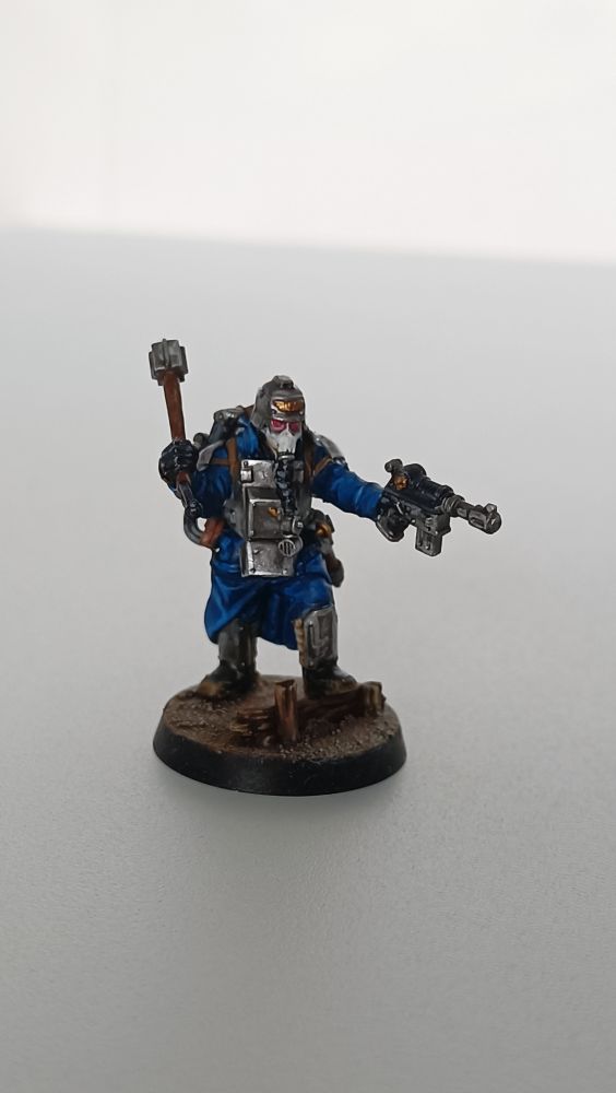 Foto de una miniatura de un soldado krieg de Warhammer 40k con ropas azules, protecciones metálicas, que empuña una maza y una pistola 