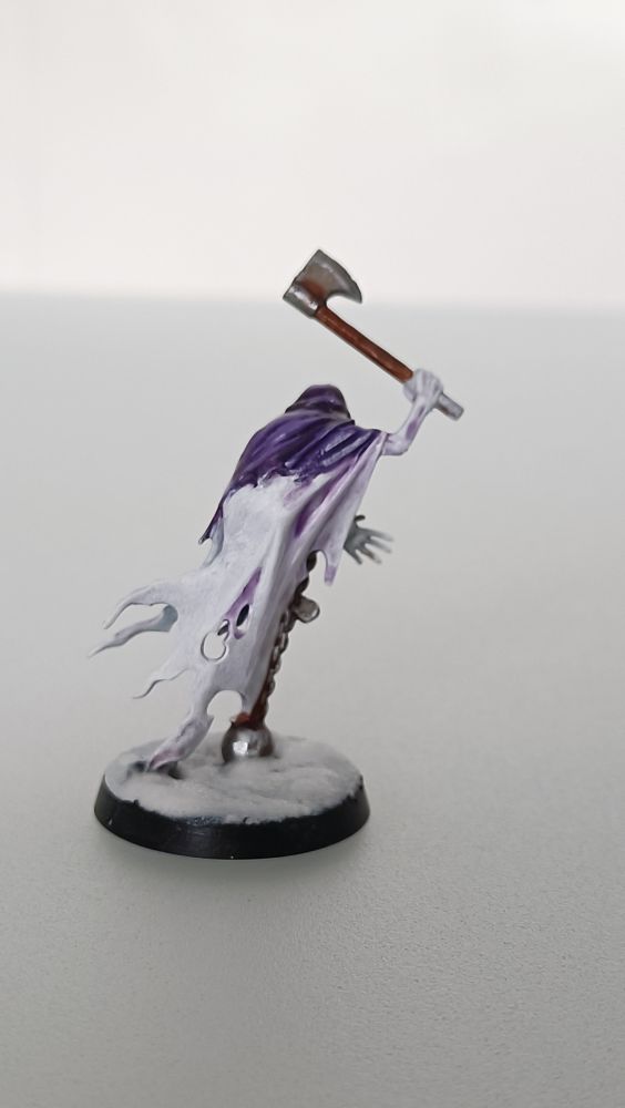 Miniatura de un fantasma de Warhammer Age of Sigmar con harapos blancos y capucha morada, que arrastra una bola y blande un hacha 