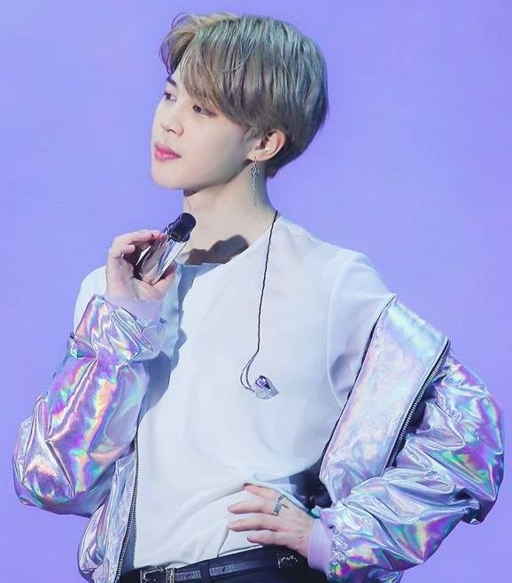 Blond Jimin posing with a hand on his hip. He's wearing a white shirt and a gray reflective bomber jacket that's hanging off his shoulder.