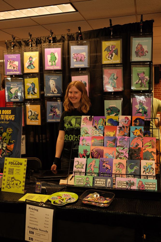 An artist poses with their table of comic art at A2CAF