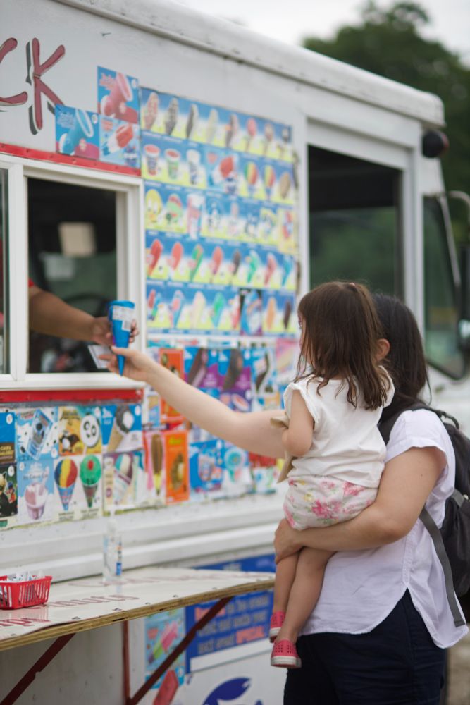A mom holds her child as she grabs ice cream from the truck.