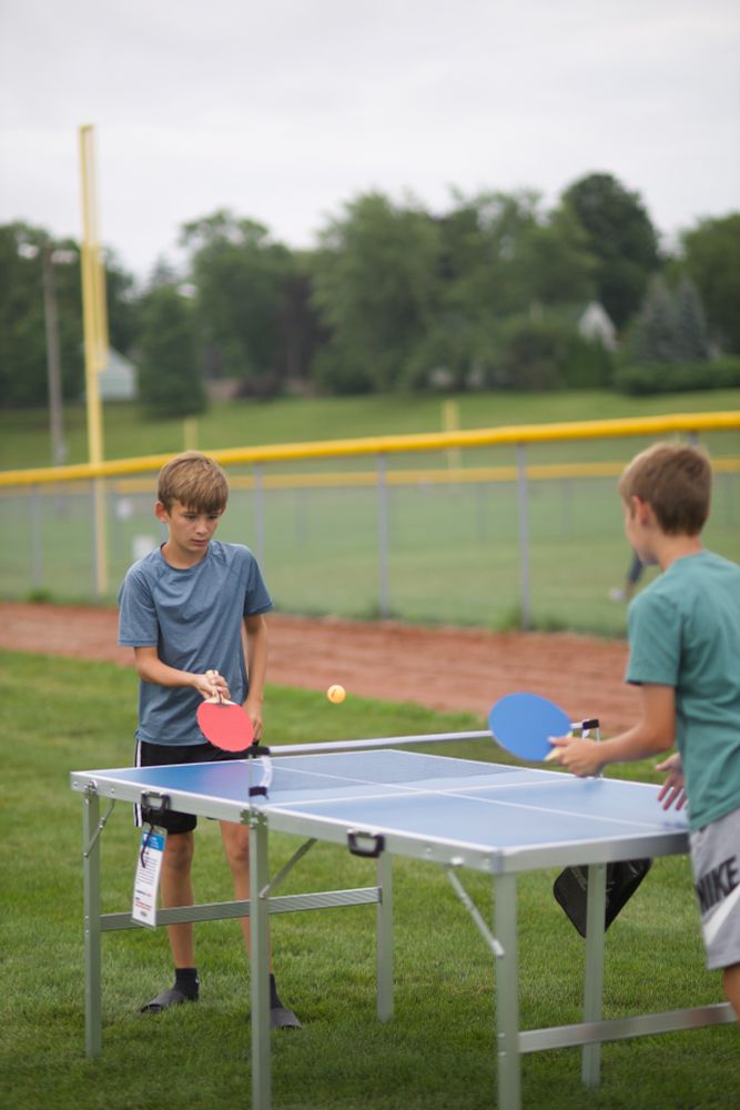Two boys play ping pong outside.