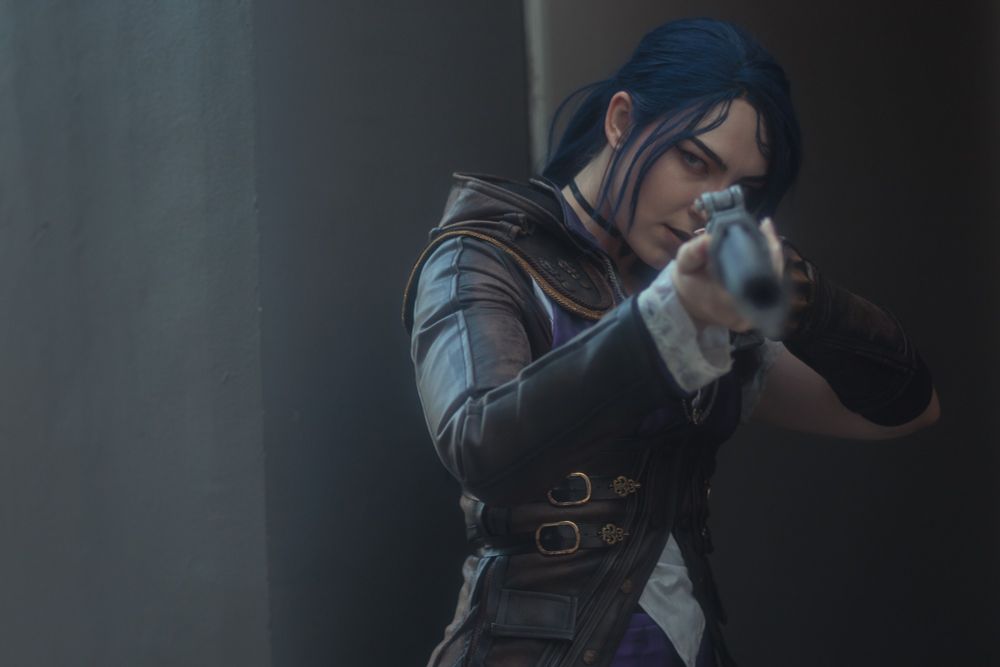 A cosplayer of Caitlyn from Arcane. She's aiming her gun at the camera.