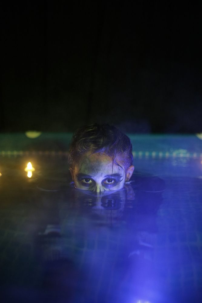 Photo of a cosplayer of Harrow from Gideon the Ninth. They are in a pool with only their eyes and above visible.

There is a fog effect from spraying directly at the water surface. Candles are floating behind.