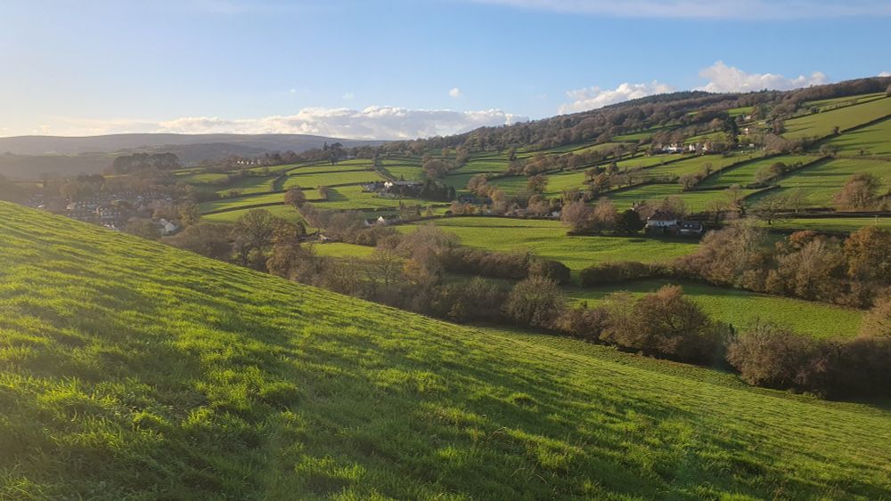 View across green fields bathed in sunshine to Dartmoor in the distance. 