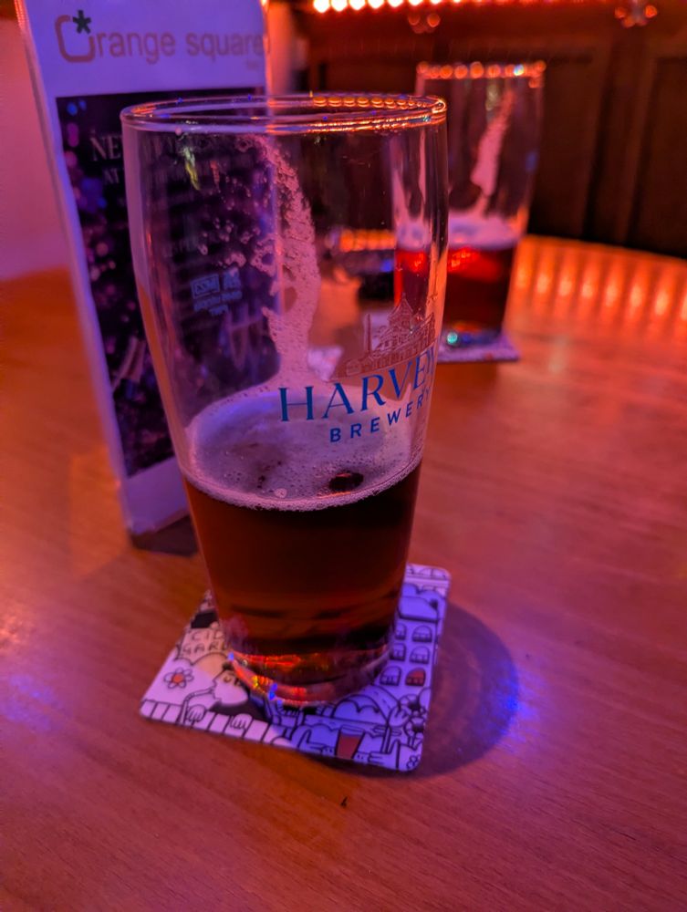 A mostly drunk pint of Harvey's Best in a Harvey's branded pint glass, in front of a similar pint, on a table in a bar. Everything is bathed in red light