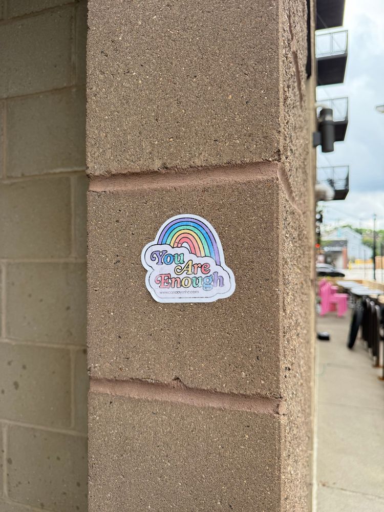Sticker on a cement wall with a rainbow and the words “you are enough”