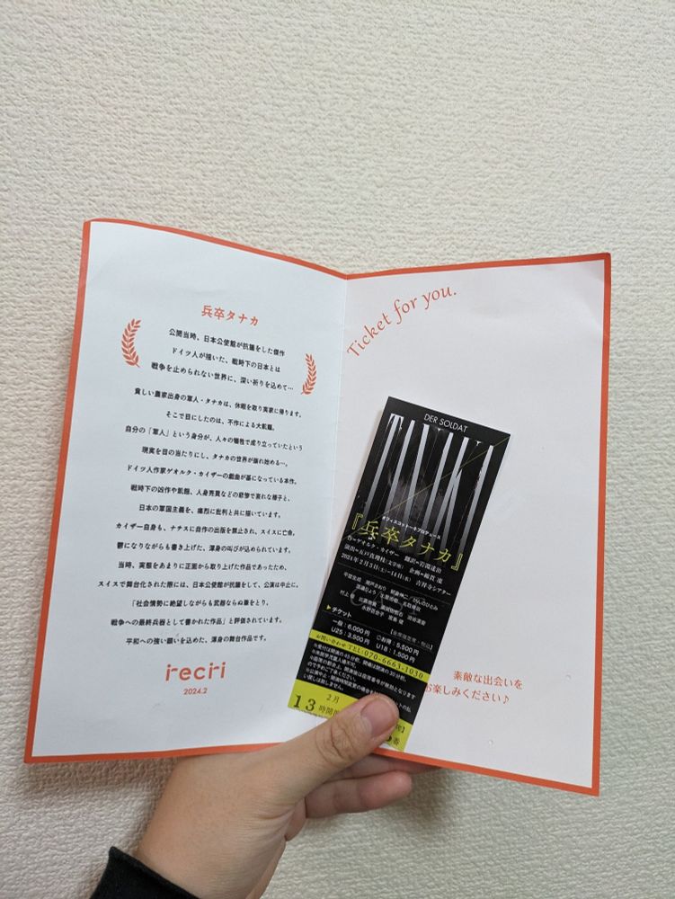 recriの解説レターと中に入っていた「兵卒タナカ」のチケットを左手で持っている