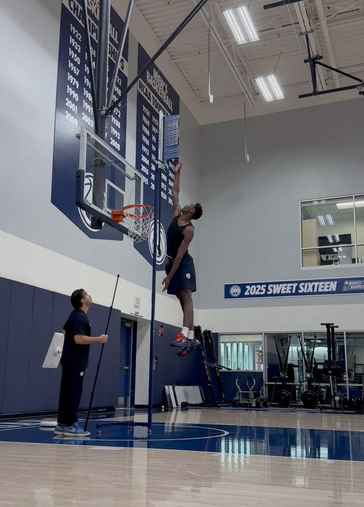 AJ Dybantsa with his chin over the rim touching a measuring thingy with his hand about a foot higher than the top of the backboard.