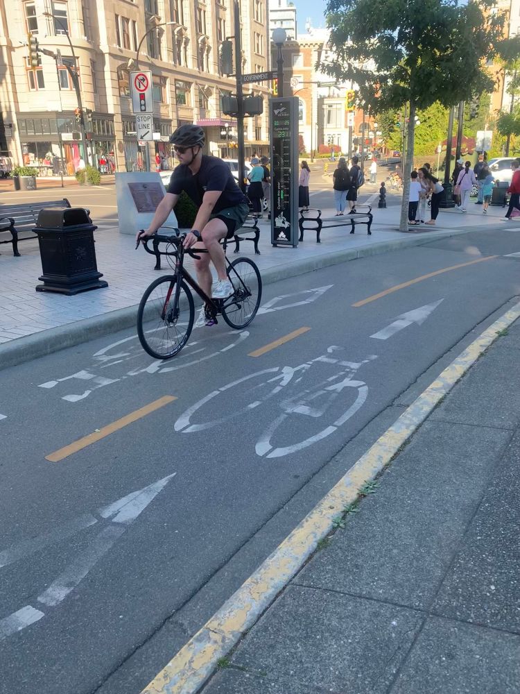 A person bikes past a Victoria protected bike lane with a counter showing over 2300 bikes so far today!