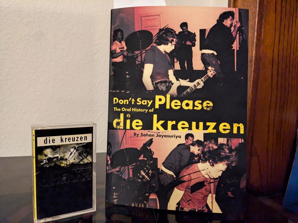 On the right, Don't Say Please: the Oral History of die kreuzen by Sahan Jayasuriya.  On the left, a cassette copy of the first die kreuzen album.