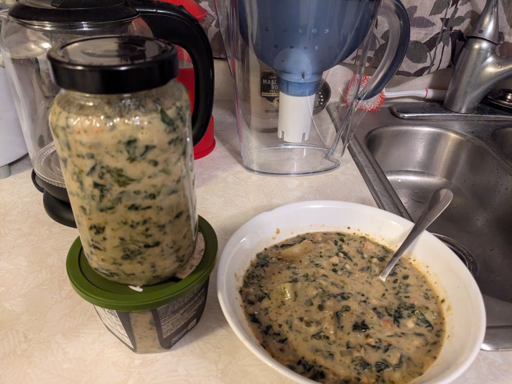 A bowl of sausage, potato, and spinach soup. Leftovers in a jar and a reused grocery store soup package.