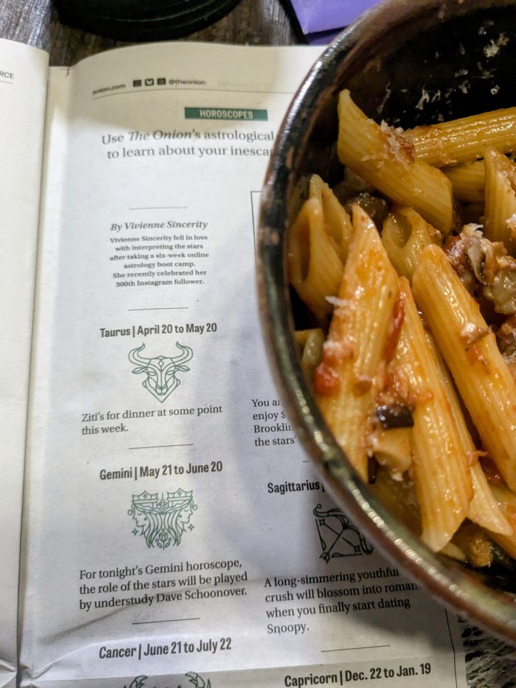 A bowl of PENNE sitting on top of an industry-leading newspaper. 