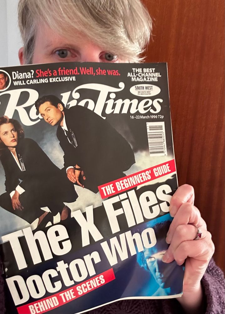A middle-aged woman holding up a copy of the Radio Times with a cover that is split between The X-Files and Doctor Who. 