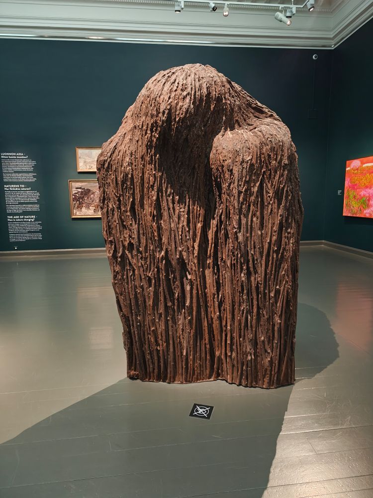 A photo of a modern art sculpture that looks like a shambling mound that wants to hug you... Maybe absorb you . Who knows. 

It's a woody brown colour. 