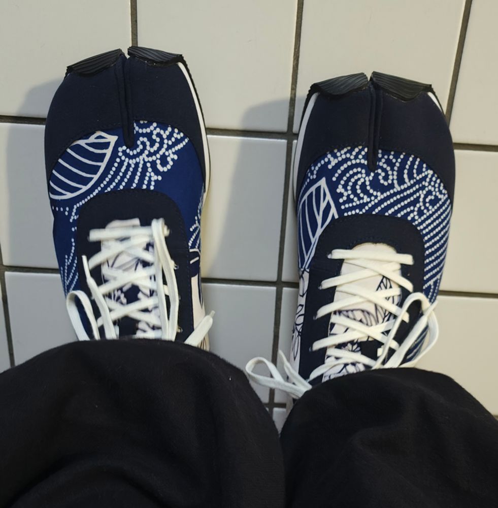 A photo of a pair of tabi shoes made from recycled Kimono - there is a white wave-like pattern on a navy background. 