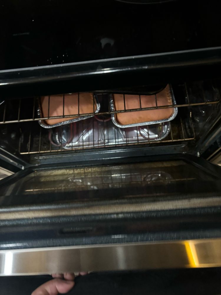 a picture of an opened oven with 2 aluminum pans of pink cake 